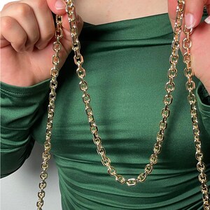 May include: A gold chain necklace with a thick, rounded link design. The chain is worn by a person wearing a green shirt.