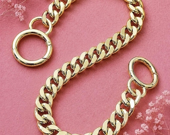 May include: A gold-toned metal chain strap featuring thick, interlocking curb links. The chain is finished with a circular spring-gate ring at each end, designed for attachment to bags or accessories, showcasing a polished, reflective surface.