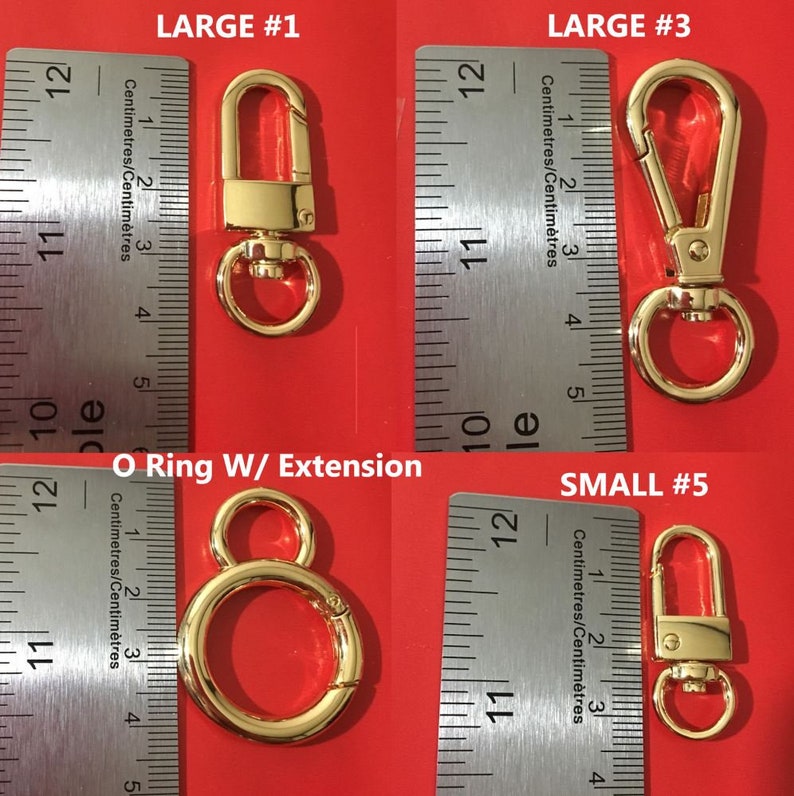 May include: Four gold-colored metal clasps and a ring with an extension. The clasps are different sizes and are labeled "LARGE #1", "LARGE #3", and "SMALL #5". The clasps are measured in centimeters.