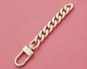 May include: A gold-toned metal chain strap featuring a series of interlocking curb links. One end of the chain is attached to a rectangular swivel lobster clasp, which is designed to rotate and provide a secure attachment point for various items.