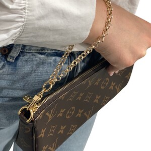 May include: A brown and tan leather purse with a gold chain strap. The purse has a monogram pattern and a zipper closure.