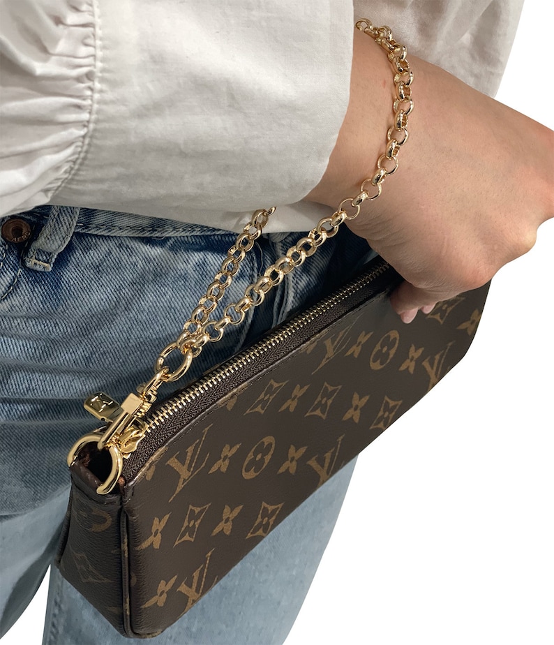 May include: A brown and tan leather purse with a gold chain strap. The purse has a monogram pattern and a zipper closure.