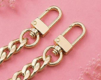 May include: Two gold-toned metal chain straps featuring polished, interlocking oval links. Each chain terminates in a rectangular swivel lobster clasp mechanism, designed for secure attachment to bags or accessories with a bright, reflective finish.