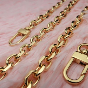 May include: Three gold chain straps with lobster clasps. The chains are different lengths and thicknesses. The chains are on a pink fuzzy surface.