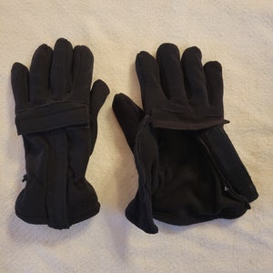 Op de afbeelding: Een paar zwarte fleece handschoenen met een klittenbandsluiting aan de pols.