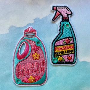 May include: Embroidered patches in the shape of cleaning product bottles. One patch reads "Bullshit Remover" and the other reads "Fuckboi Repellent". Both patches are pink and teal with floral accents and have teal eyelets.