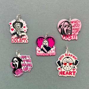May include: Five horror-themed keychains with silver rings. Each keychain features a different character, including Freddy Krueger, Michael Myers, and Ghostface, with phrases like "Man of your Dreams" and "You Slay My Heart" in pink and white.