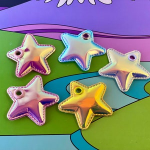 May include: Five iridescent star-shaped patches with a metallic sheen. Each star has a different color, including pink, blue, and yellow, and a stitched border. They have a small hole at the top for attaching to items.