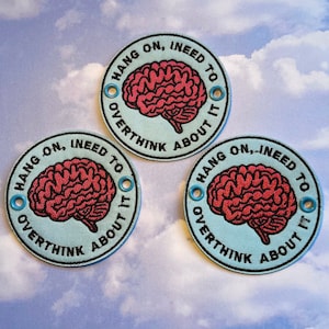 May include: Three round patches with the text "HANG ON, I NEED TO OVERTHINK ABOUT IT". Each patch features a red brain graphic. The patches have a light blue background and are bordered with black stitching.