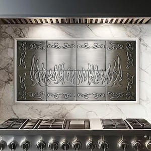 May include: A stainless steel range with six burners and two ovens. The range has a black hood above it and a decorative tile backsplash with a flame design. The range is in a kitchen with white cabinets and marble countertops.