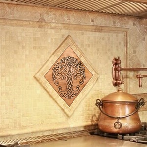 May include: A copper-coloured tile backsplash with a Celtic tree of life design in a diamond shape. The backsplash is installed above a stainless steel stovetop with black burner grates.