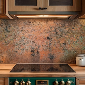 May include: A kitchen interior with wooden cabinets and a copper-effect splashback. The green stove has brass fittings, and the wooden worktop holds jars and a black hob. The cabinets have glass-fronted doors.