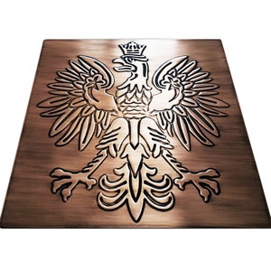 Puede incluir: Una placa de metal de color cobre con un diseño en relieve detallado del emblema nacional polaco, un águila blanca coronada, sobre un fondo de metal cepillado.