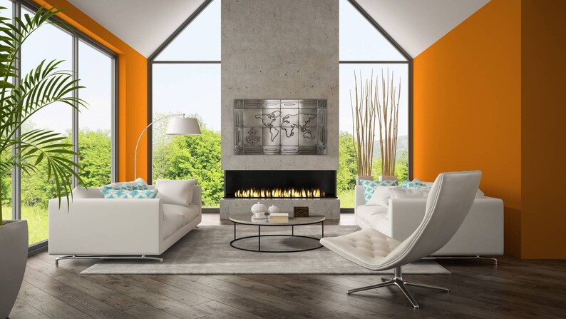 May include: A modern living room with white sofas, a gray rug, and a black coffee table. The room features an orange accent wall, large windows, and a fireplace with a metal world map art piece above it. A white chair is in the foreground.
