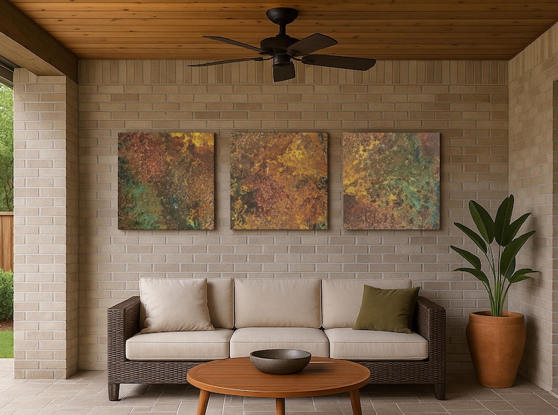May include: An outdoor seating area with a brown wicker sofa and beige cushions. A round wooden coffee table sits in front of the sofa. Three abstract artworks hang on the brick wall. A potted plant and ceiling fan are also present.