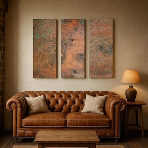 May include: A living room scene featuring a brown leather Chesterfield sofa with two beige throw pillows, a wooden coffee table, and a side table with a lamp. Three rectangular abstract art pieces hang on the wall, above the sofa.