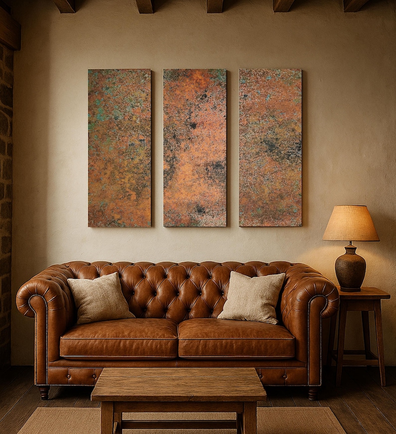 May include: A living room scene featuring a brown leather Chesterfield sofa with two beige throw pillows, a wooden coffee table, and a side table with a lamp. Three rectangular abstract art pieces hang on the wall, above the sofa.