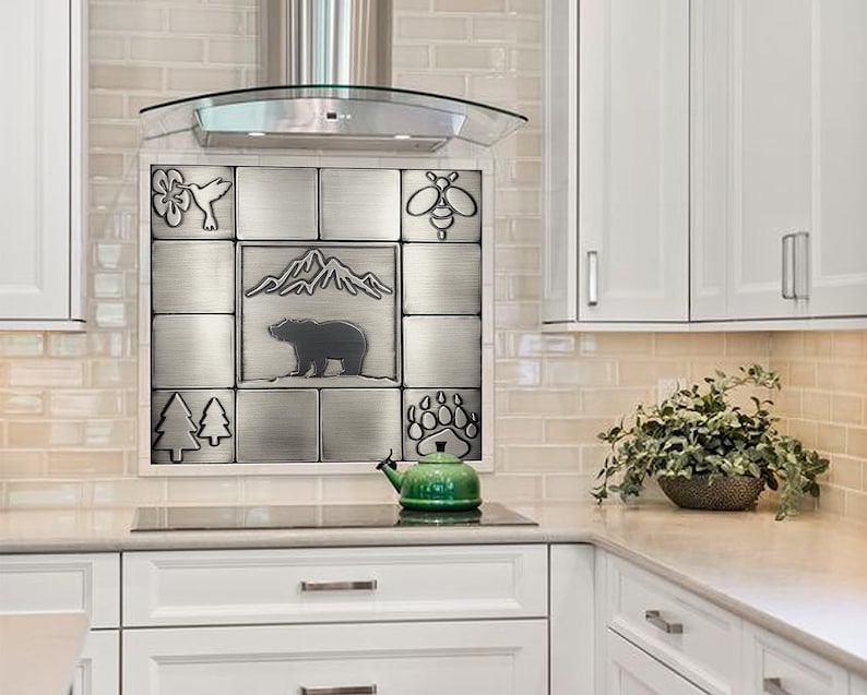 Puede incluir: Un protector contra salpicaduras de acero inoxidable con un dise&ntilde;o de azulejos que presenta un oso, monta&ntilde;as, &aacute;rboles, una abeja y un colibr&iacute;. El protector contra salpicaduras est&aacute; instalado sobre una estufa en una cocina.