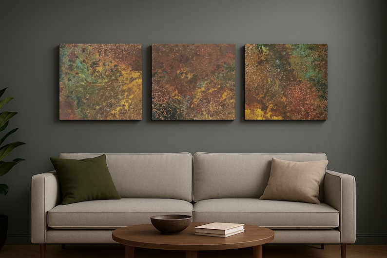 May include: Three square abstract artworks with a textured, mottled appearance in shades of brown, green, and yellow. The art hangs above a light-coloured sofa with olive and tan cushions.