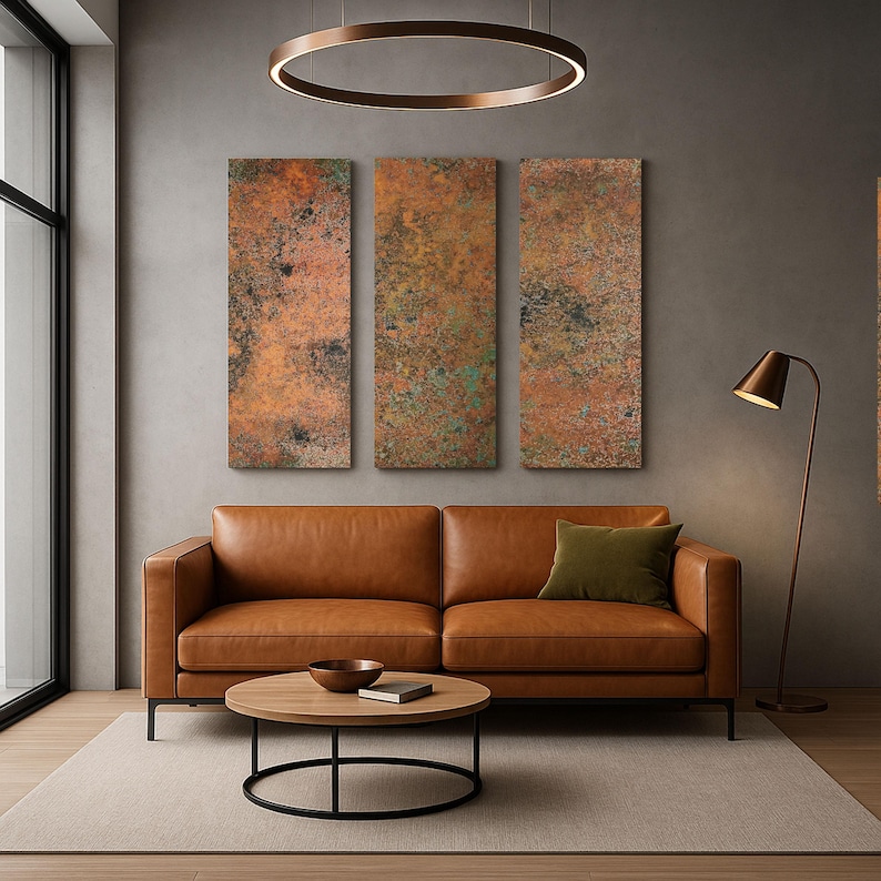 May include: A modern living room featuring a brown leather sofa, a round wooden coffee table with a black metal base, and three rectangular wall art pieces with a textured, copper-colored finish. An olive green pillow adds a pop of color.