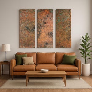 May include: Three rectangular wall art panels with a textured, mottled copper-colored finish. The panels hang above a brown leather sofa with green and tan throw pillows. A wooden coffee table and a potted plant complete the living room scene.