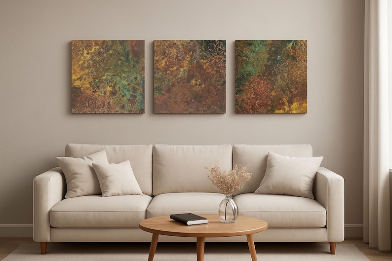 May include: Three square abstract art pieces with textured surfaces in shades of brown, green, and yellow hang above a beige sofa. The room features a round wooden coffee table and neutral-toned decor.