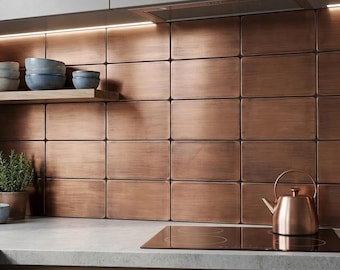 May include: A kitchen backsplash featuring rectangular metallic copper tiles with a brushed finish. A wooden shelf holds stacked blue bowls, while a copper tea kettle sits on a black glass stovetop. The area is illuminated by under-cabinet lighting.