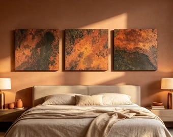 May include: Three square wall art panels featuring abstract textures in shades of burnt orange, copper, and dark charcoal. The artwork is displayed horizontally above a bed with neutral-toned bedding and two matching bedside lamps.