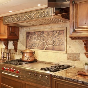 May include: A stainless steel gas stove with four burners and a copper pot on the stovetop. The stove is in a kitchen with brown cabinets and a decorative tile backsplash featuring a tree design.