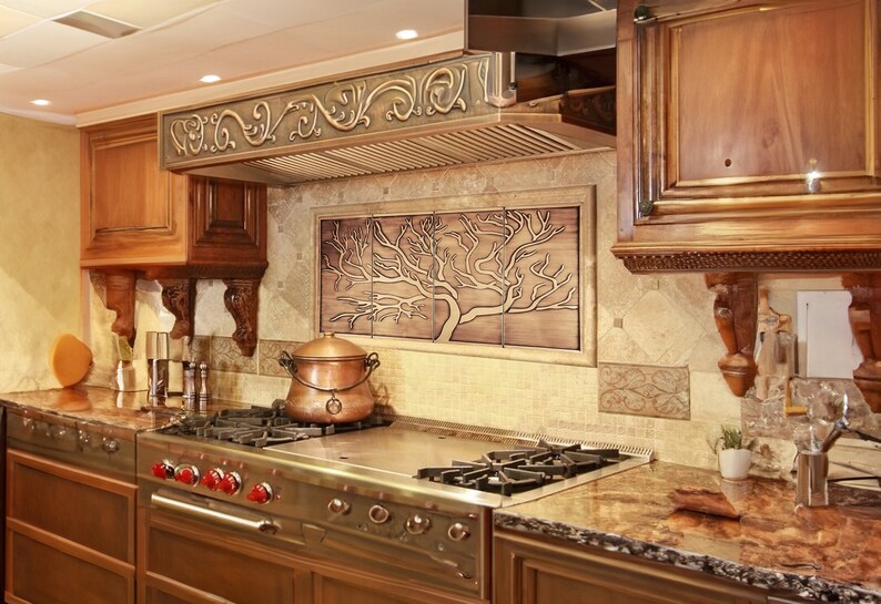 May include: A stainless steel gas stove with four burners and a copper pot on the stovetop. The stove is in a kitchen with brown cabinets and a decorative tile backsplash featuring a tree design.