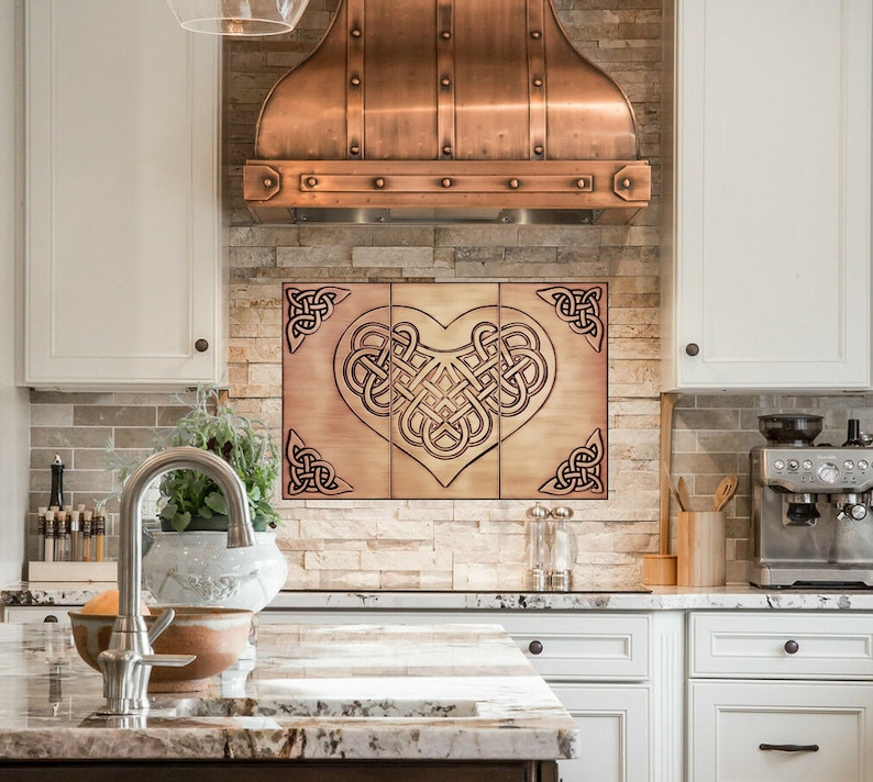 May include: A copper kitchen range hood with a Celtic knot heart design backsplash. The backsplash is made of tiles with a copper finish.