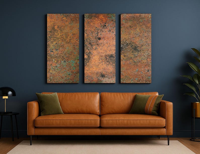 May include: A living room scene featuring a brown leather sofa with olive green throw pillows. Above the sofa are three rectangular wall art pieces with a textured, copper-colored finish. The wall is painted a dark blue.