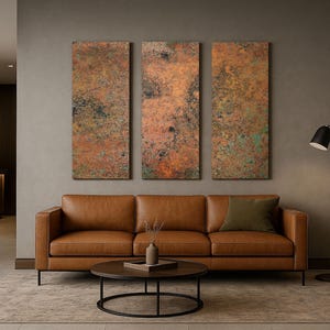 May include: A modern living room setup featuring a brown leather sofa, a round coffee table, and three abstract wall art pieces with copper and green tones. A black floor lamp and a rug complete the decor.