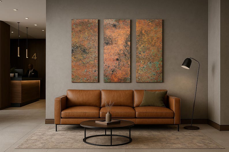 May include: A modern living room setup featuring a brown leather sofa, a round coffee table, and three abstract wall art pieces with copper and green tones. A black floor lamp and a rug complete the decor.