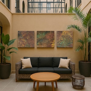 May include: An outdoor seating area with a dark grey wicker sofa, beige cushions, a round wooden coffee table, and a woven side table. Three abstract artworks are mounted above the sofa, with potted plants on either side.