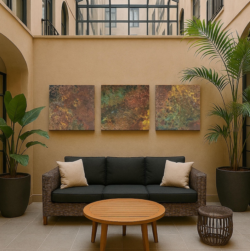 May include: An outdoor seating area with a dark grey wicker sofa, beige cushions, a round wooden coffee table, and a woven side table. Three abstract artworks are mounted above the sofa, with potted plants on either side.