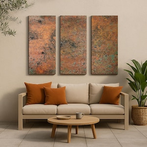 May include: Three rectangular wall art panels with a textured, weathered copper appearance. The panels hang above a beige sofa with orange throw pillows. A round wooden coffee table and a potted plant complete the outdoor living space.