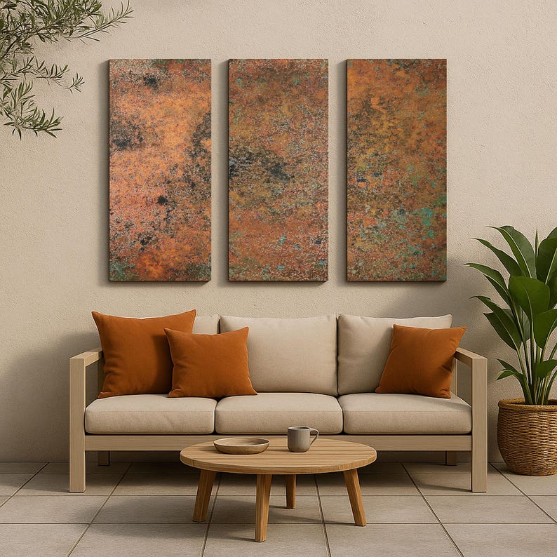 May include: Three rectangular wall art panels with a textured, weathered copper appearance. The panels hang above a beige sofa with orange throw pillows. A round wooden coffee table and a potted plant complete the outdoor living space.