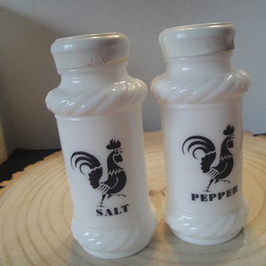 Pode incluir: Saleiro e pimenteiro brancos com um design de galo preto. O saleiro diz "SALT" e o pimenteiro diz "PEPPER".