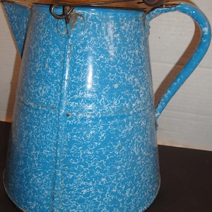 May include: A blue and white speckled enamelware pitcher with a wooden handle and lid. The pitcher has a vintage look and is perfect for serving beverages.
