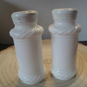 Pode incluir: Dois saleiros e pimenteiros de vidro de leite branco com um design de corda ao redor do meio.