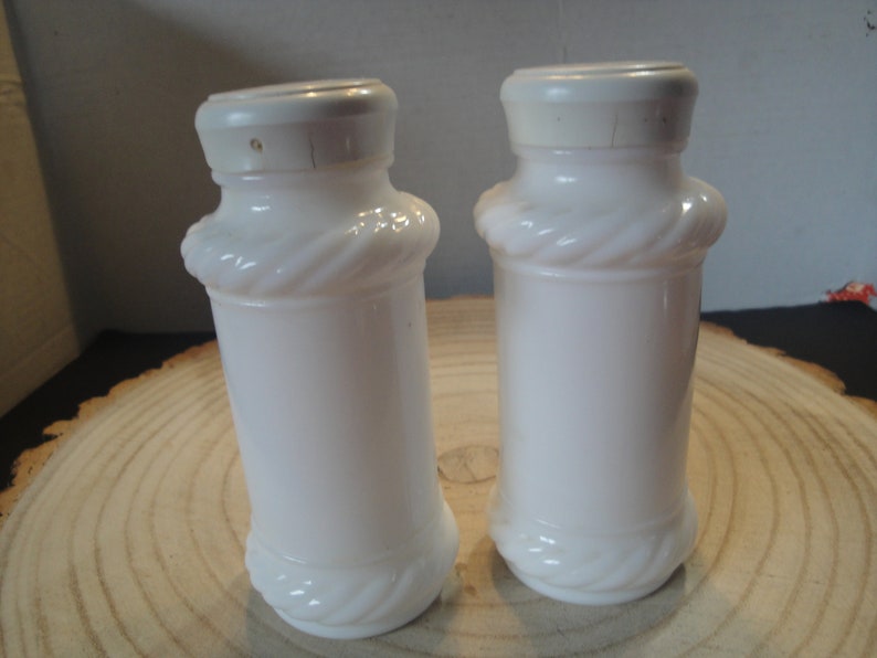 Pode incluir: Dois saleiros e pimenteiros de vidro de leite branco com um design de corda ao redor do meio.