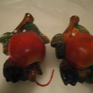 May include: Two ceramic wall decor pieces shaped like apples with green leaves and brown stems. The apples are red and have a glossy finish.