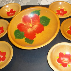 May include: A wooden serving set featuring a large oval tray and six smaller bowls. Each piece is painted with a vibrant red hibiscus flower design with green leaves, set against a light brown background.