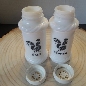 Pode incluir: Saleiro e pimenteiro de cer&acirc;mica branca com desenhos de galo preto. Os saleiros t&ecirc;m um design de corda em torno do meio e dizem "SALT" e "PEPPER" na frente.