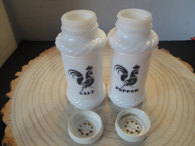 Pode incluir: Saleiro e pimenteiro de cer&acirc;mica branca com desenhos de galo preto. Os saleiros t&ecirc;m um design de corda em torno do meio e dizem "SALT" e "PEPPER" na frente.
