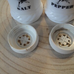 Pode incluir: Saleiro e pimenteiro de cer&acirc;mica branca com silhuetas de galos pretos e as palavras "SALT" e "PEPPER" impressas neles. Os saleiros t&ecirc;m um furo na parte superior para dispensar sal e pimenta.