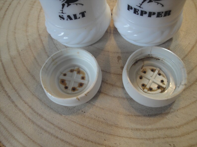 Pode incluir: Saleiro e pimenteiro de cer&acirc;mica branca com silhuetas de galos pretos e as palavras "SALT" e "PEPPER" impressas neles. Os saleiros t&ecirc;m um furo na parte superior para dispensar sal e pimenta.