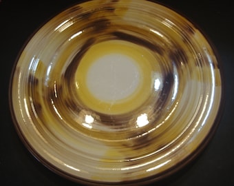 May include: A large, round, ceramic plate with a swirling pattern of brown, yellow, and white glaze. The plate has a glossy finish.