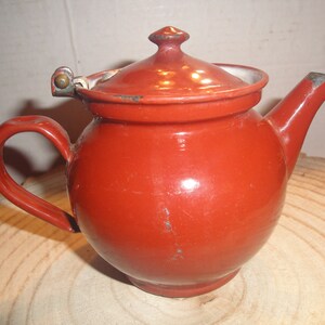 May include: A small, red enamel teapot with a hinged lid and a handle. The teapot has a round body and a spout.